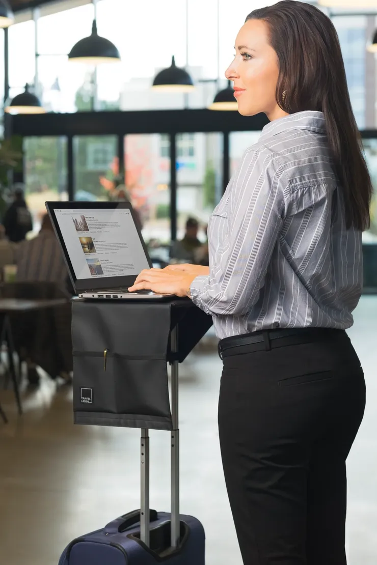 Traveler using a laptop on Travel Ledge attached to rolling luggage